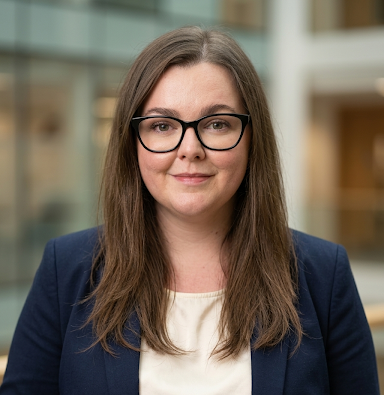 Jennifer Jackson with long brown hair, black glasses, wearing a navy blazer and cream blouse, smiling indoors.